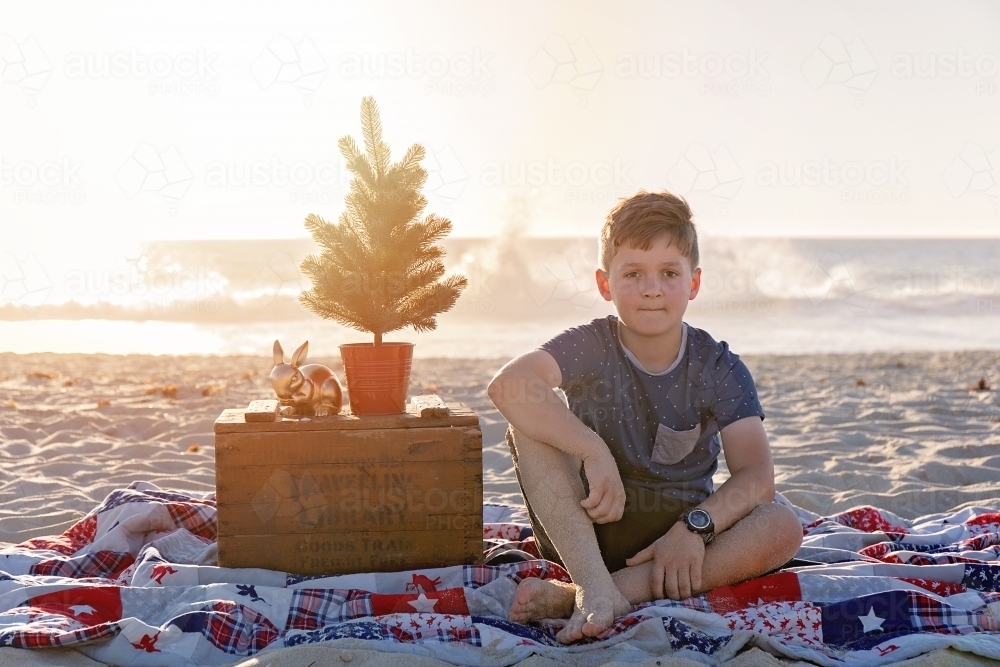 Pre Teen Boy Sitting In a Christmas Themed Setting At The Beach At Sunset - Australian Stock Image
