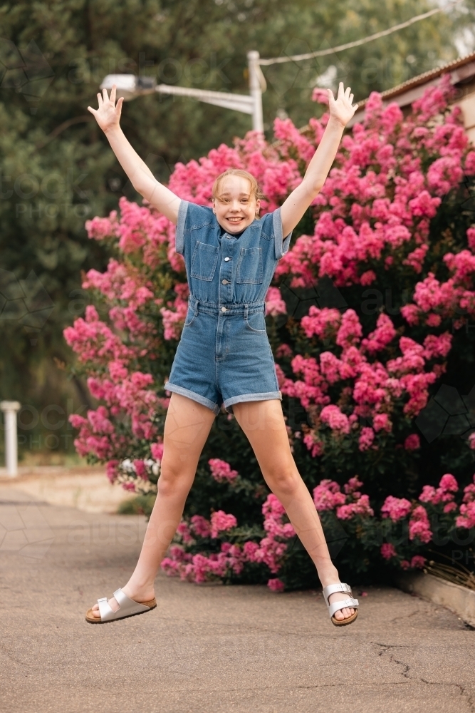 Pre-teen girl jumping in front of vibrant pink bougainvillea bush - Australian Stock Image