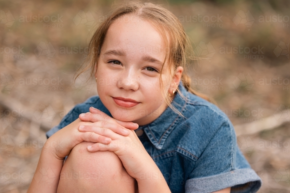 Pre-teen girl resting chin on knee in natural outdoor setting - Australian Stock Image
