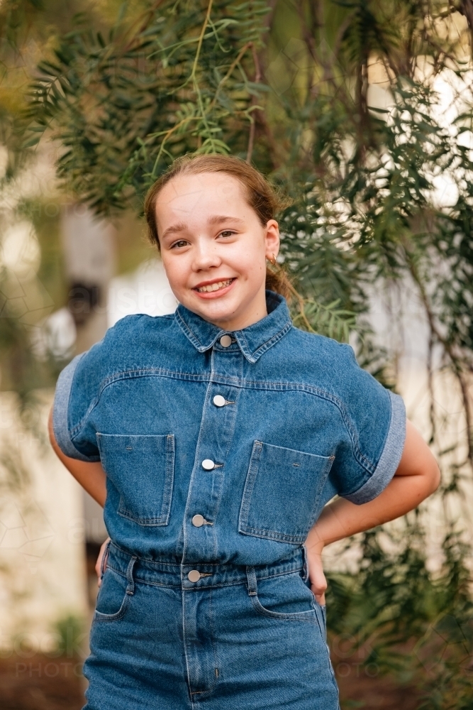 Pre-teen girl resting hands on hips in natural outdoor setting - Australian Stock Image