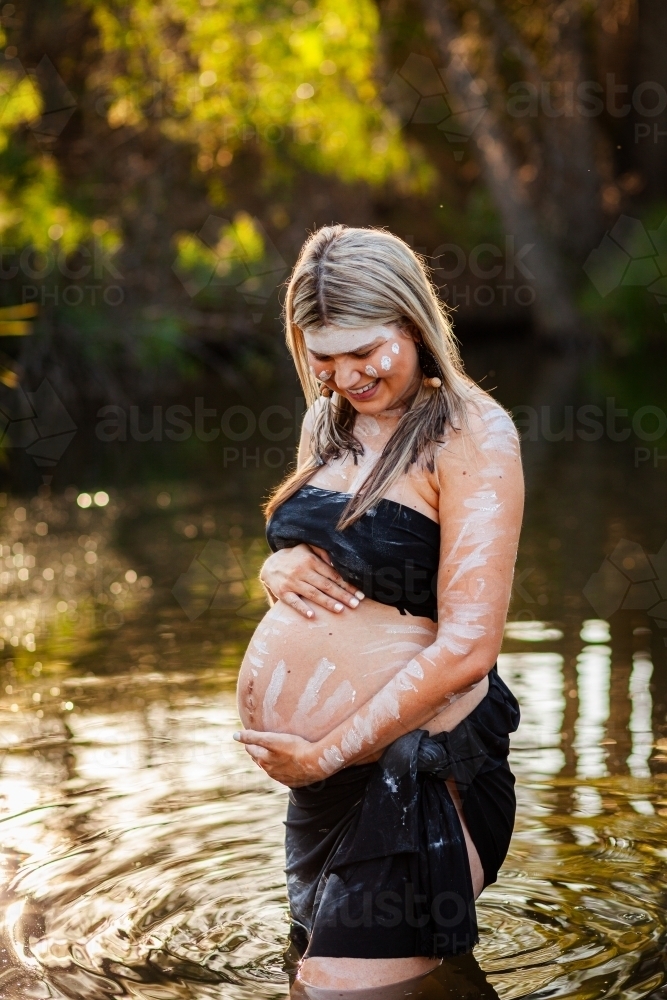 Pregnant Aboriginal Australian woman in sparkling billabong water on summer afternoon - Australian Stock Image