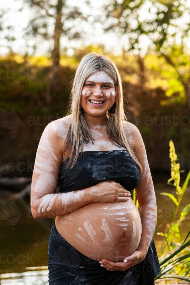 Pregnant Aboriginal Australian woman standing by creek on summer afternoon - Australian Stock Image