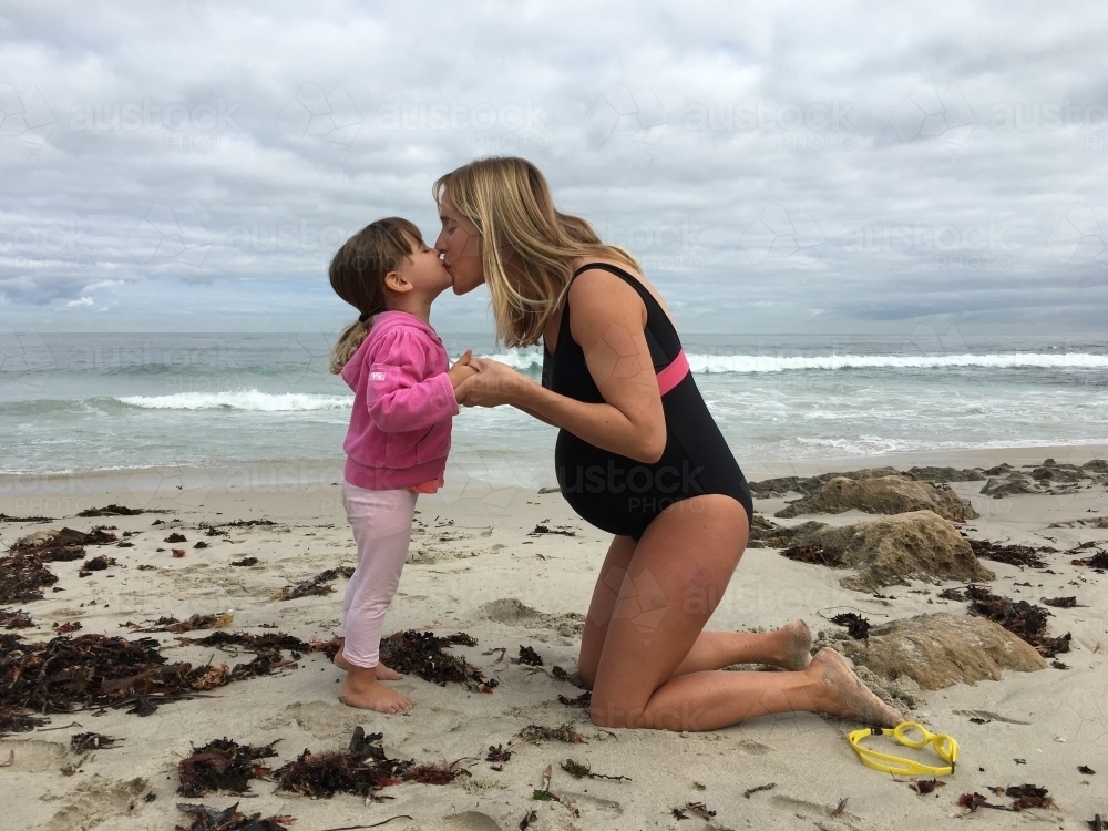 Pregnant mother kissing toddler daughter at beach on overcast day - Australian Stock Image