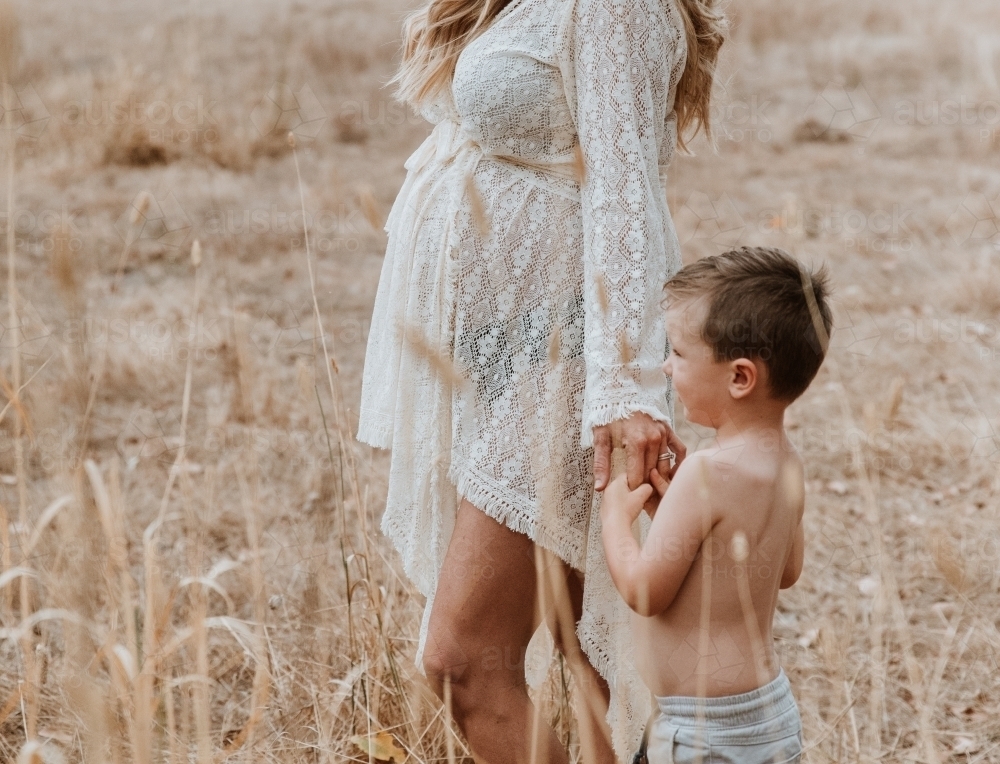 Pregnant mother walking with son through brown grass - Australian Stock Image