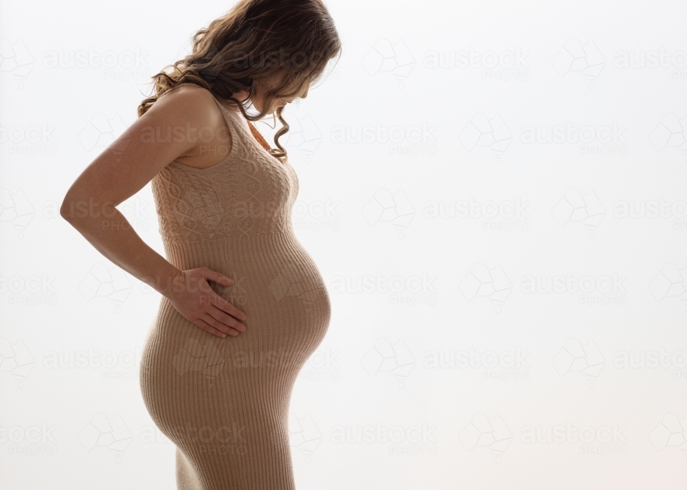 pregnant woman back lit in tight dress - Australian Stock Image