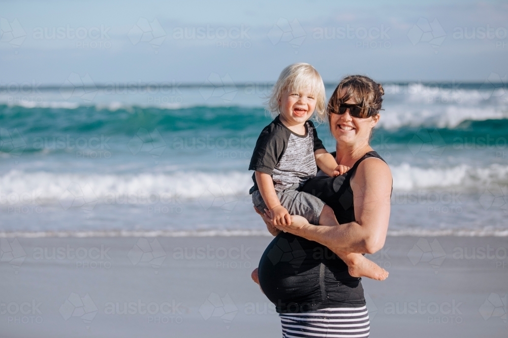 Pregnant woman, holding her toddler at the beach - Australian Stock Image