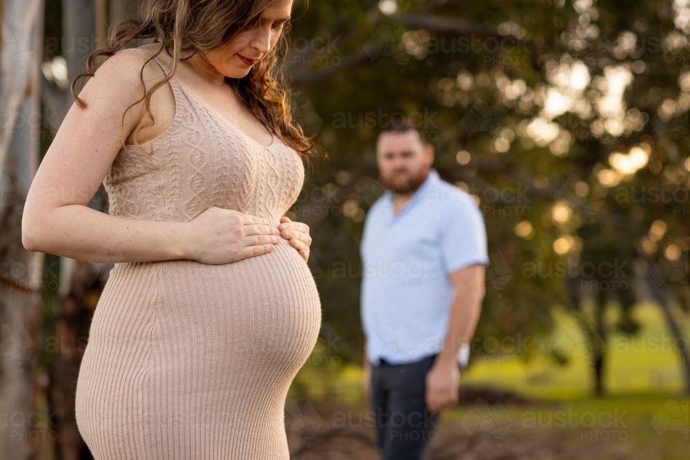 pregnant woman in foreground with her partner blurred in the background - Australian Stock Image