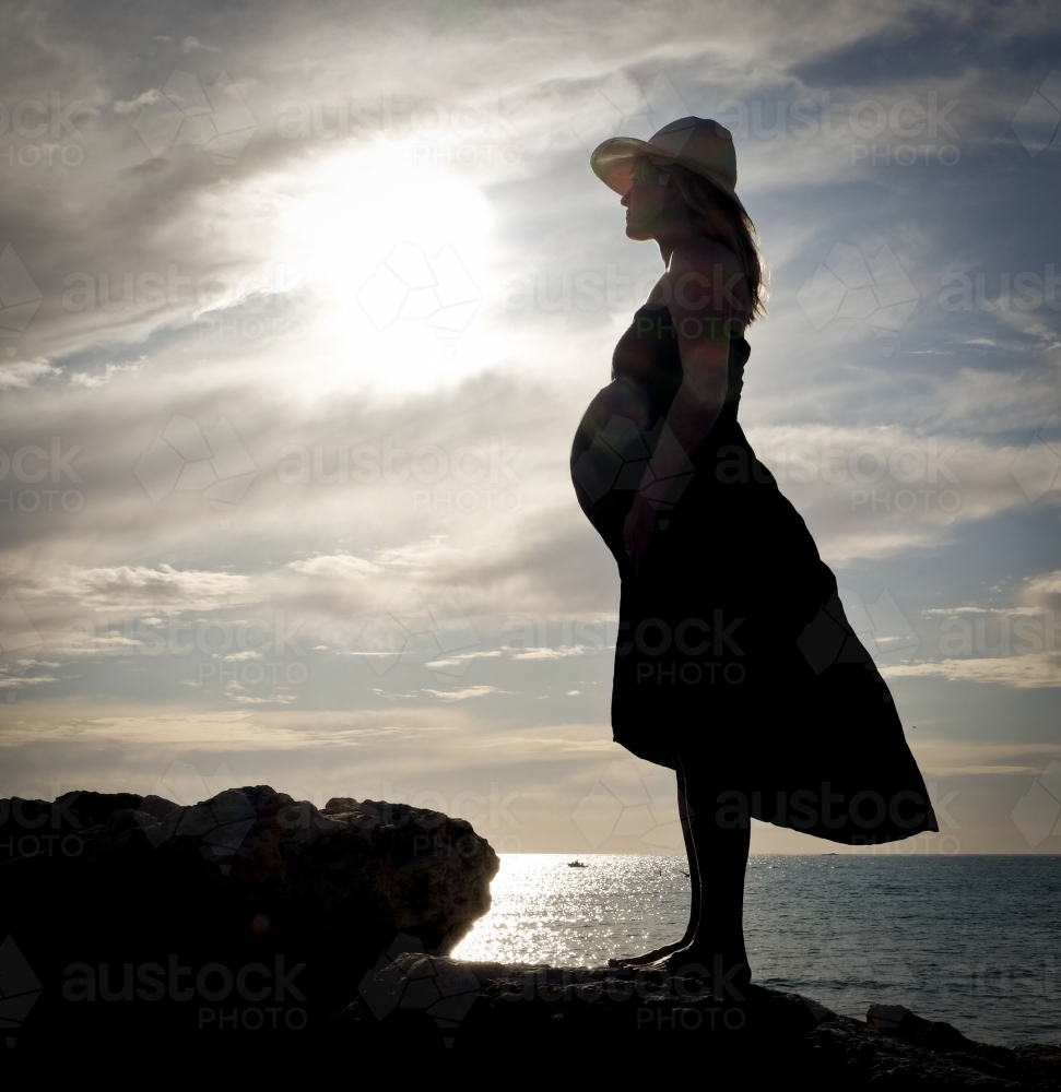 Pregnant woman standing on rock with ocean in background - Australian Stock Image