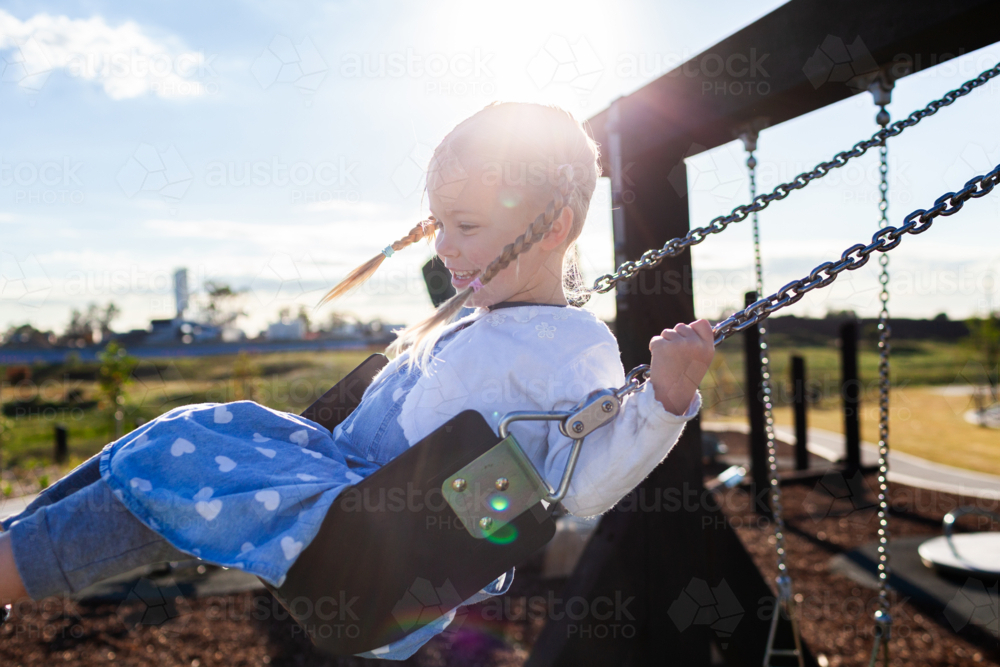 Preschool aged child swinging on swing at playground in early morning having fun by herself - Australian Stock Image