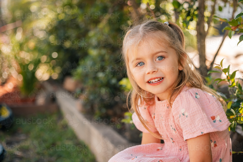 Preschool child sitting on a garden edge at kindergarten with copy space - Australian Stock Image