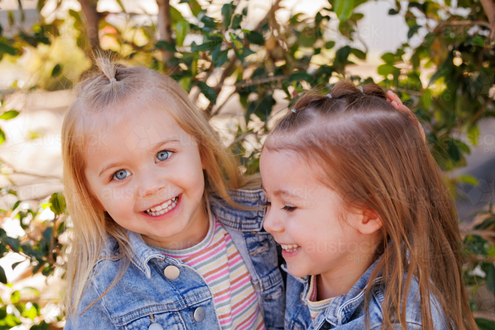 Preschooler sisters sitting together on garden edge at kindergarten - Australian Stock Image