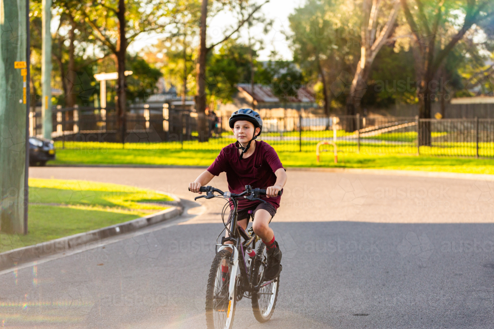 preteen boy riding alone along street in Australian country town - Australian Stock Image