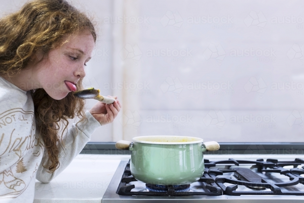 Preteen girl helping to cook over a saucepan on a stove in the kitchen - Australian Stock Image
