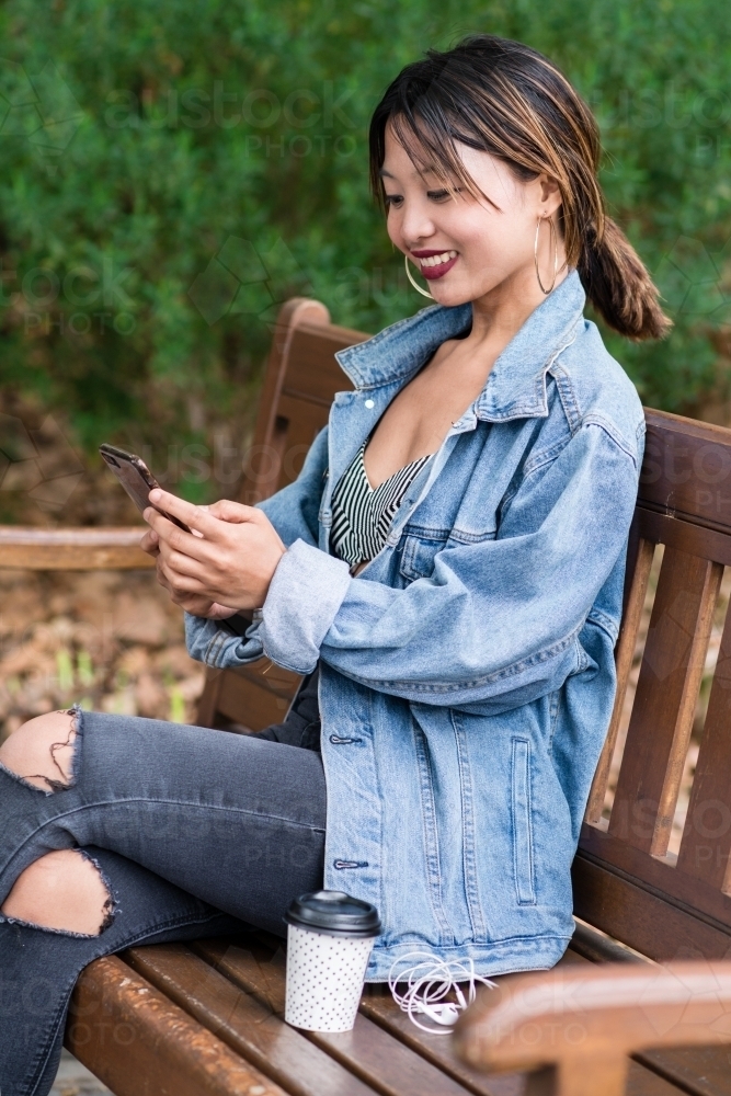 pretty asian woman looking at her phone and smiling - Australian Stock Image