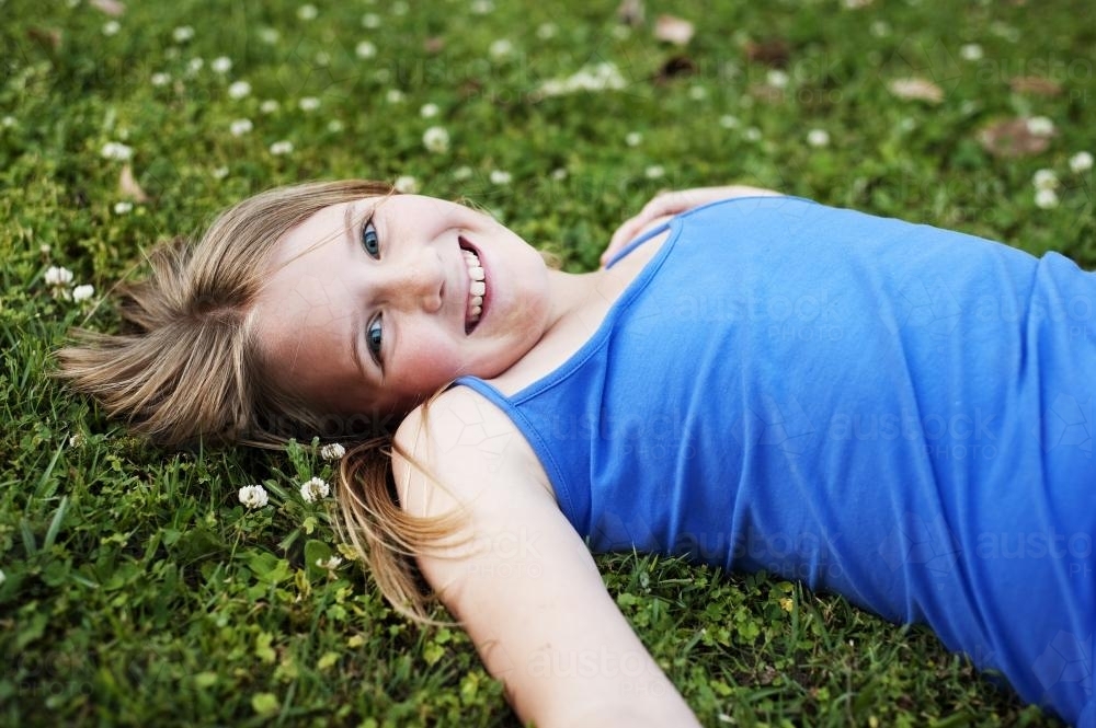 pretty blue-eyed tween girl lying in the grass - Australian Stock Image