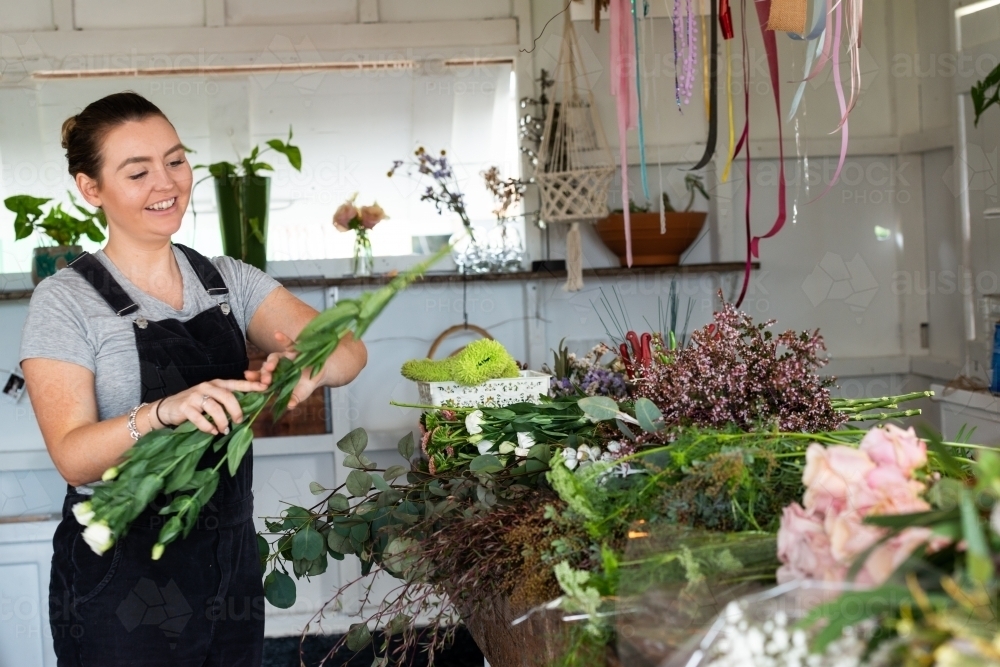 Pretty young florist at work happily preparing flowers for an event - Australian Stock Image