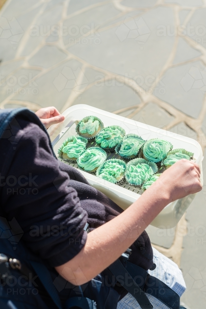 primary aged girl holding a container full of cupcakes to take to school - Australian Stock Image