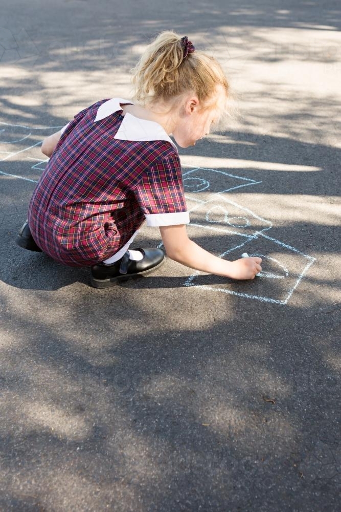 Primary school aged girl in uniform drawing chalk on asphalt - Australian Stock Image