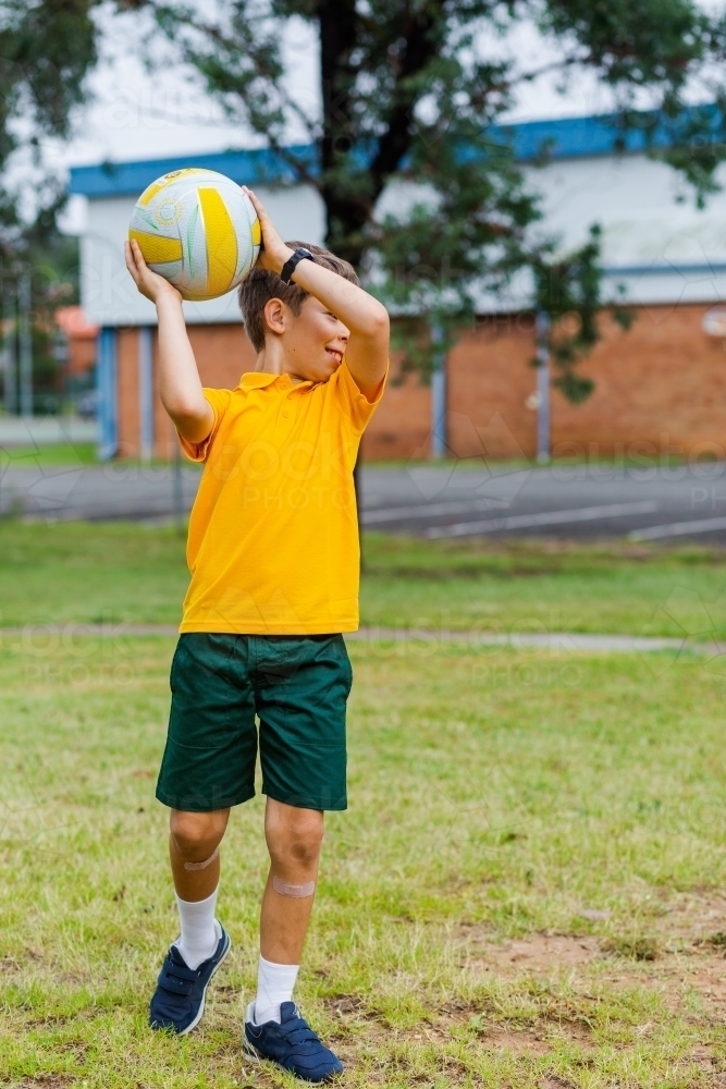 Primary school boy throwing ball outside - Australian Stock Image