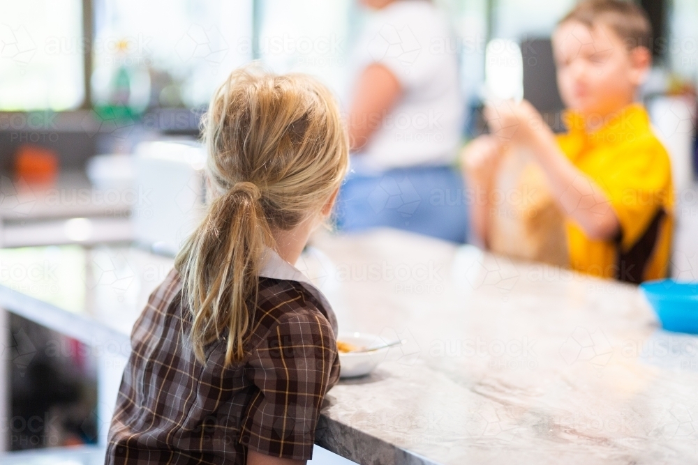 Primary school girl sitting at bench eating breakfast before school - Australian Stock Image