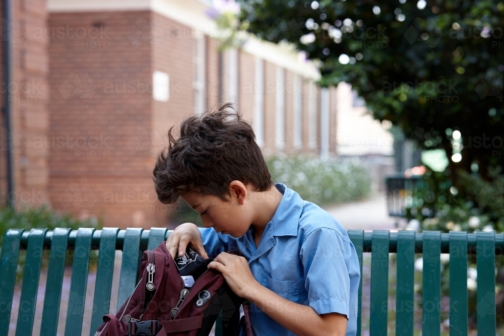 Primary school student at school looking in backpack - Australian Stock Image