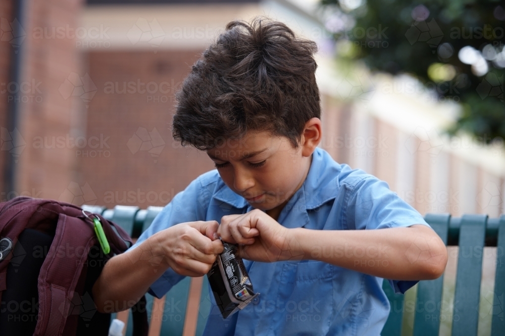 Primary school student at opening packet of food - Australian Stock Image