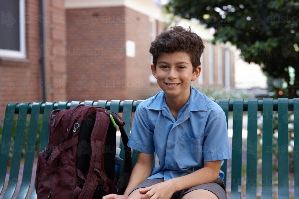 Primary school student at sitting with backpack smiling at camera - Australian Stock Image