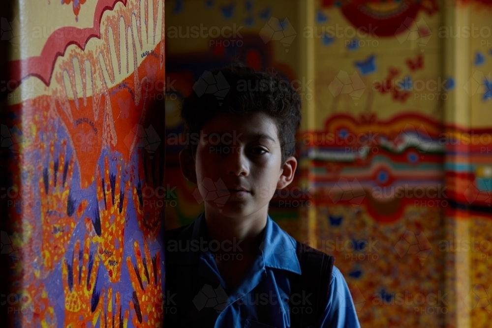 Serious primary school student in shadows of corridor with murals at school - Australian Stock Image