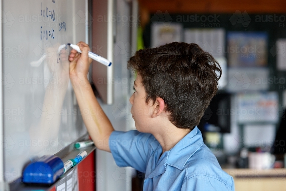 Primary school student in classroom writing on whiteboard - Australian Stock Image