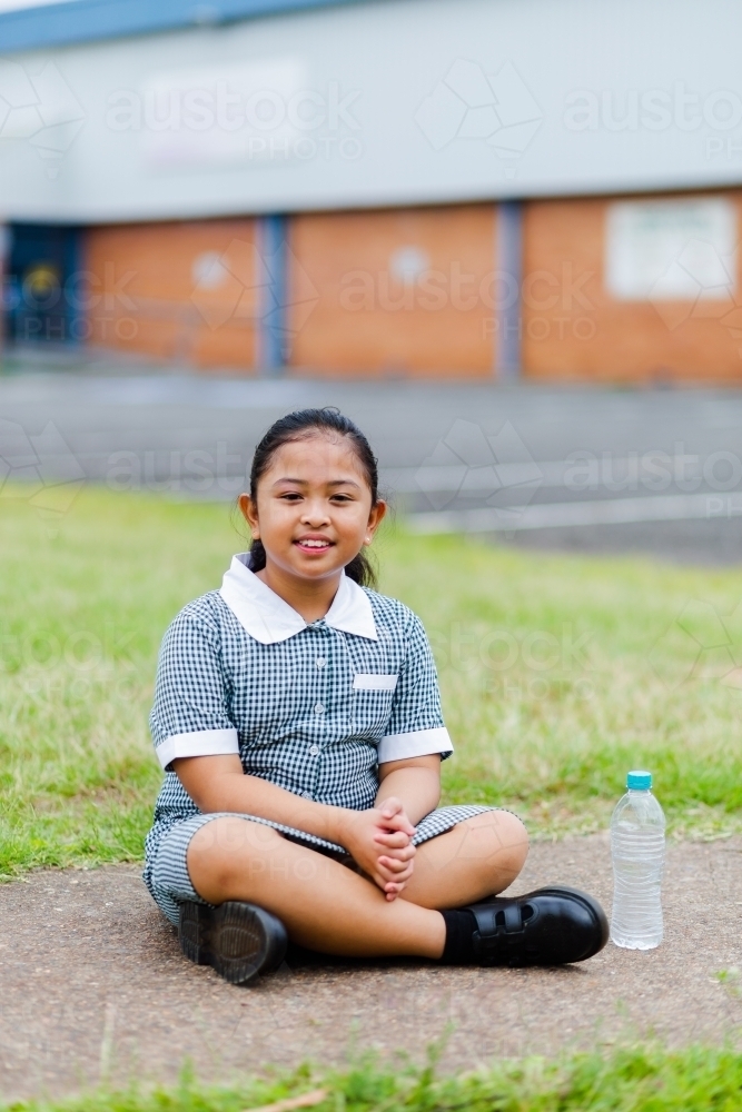 Primary school student resting on ground with drink of bottled water - Australian Stock Image