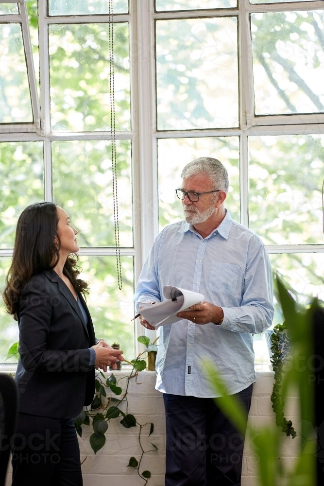 Professional business woman and man standing, discussing paperwork - Australian Stock Image