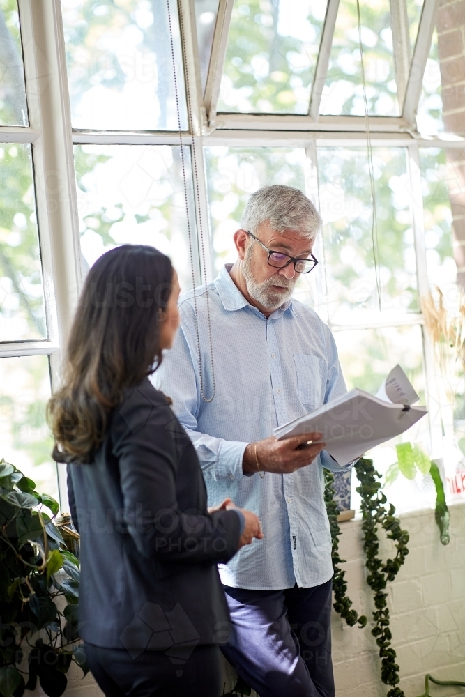 Professional business woman and man standing, discussing paperwork - Australian Stock Image