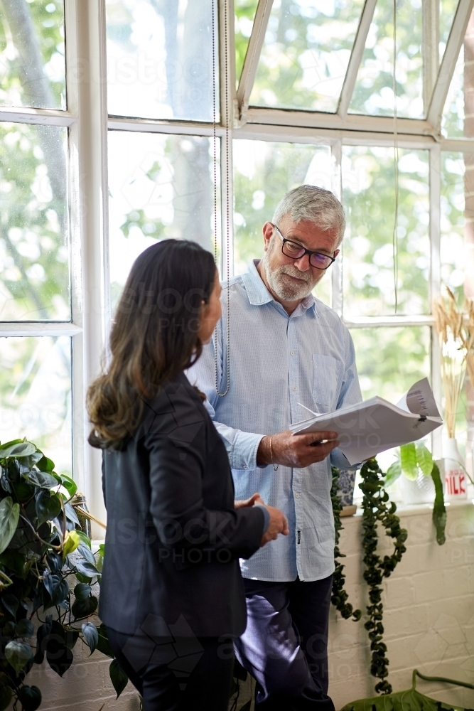 Professional business woman and man standing, discussing paperwork - Australian Stock Image