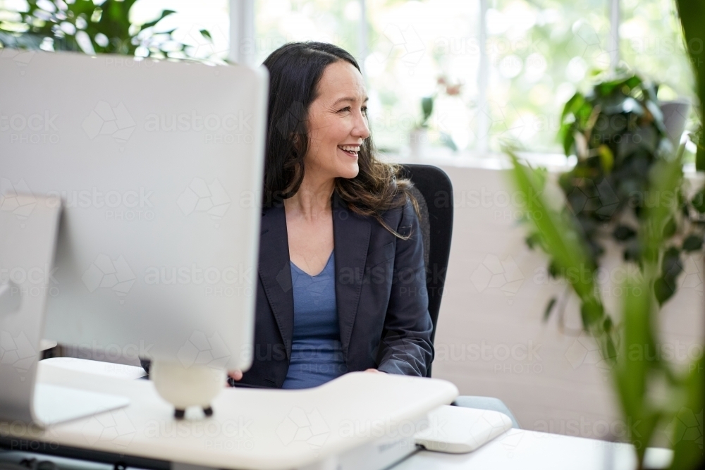 Professional business woman sitting at a computer in an office studio - Australian Stock Image