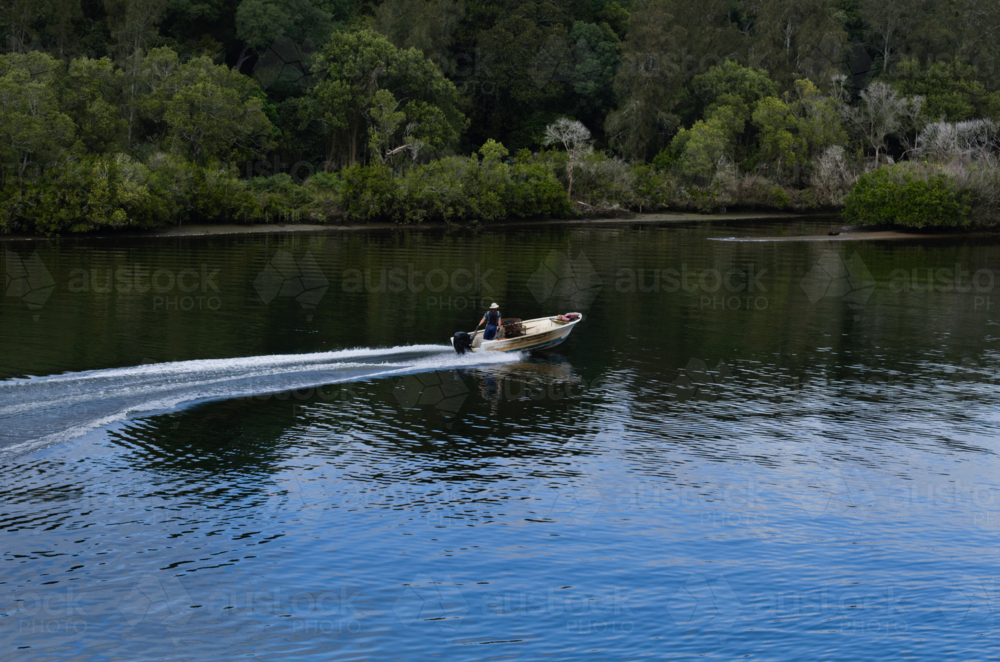 Professional fisherman speeding in boat in river with bush background - Australian Stock Image