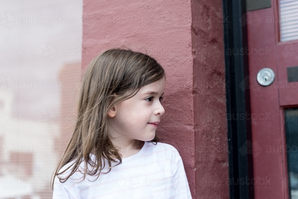 Profile of a young girl standing against a pink brick wall - Australian Stock Image