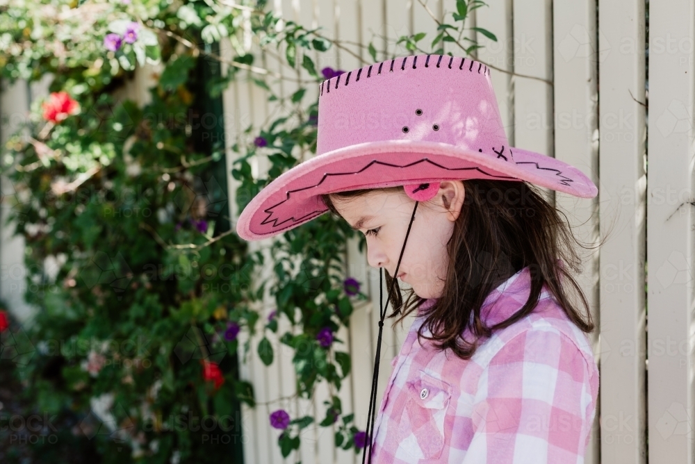Profile of happy young girl dressed up as a cowgirl wearing a pink akubra hat and pink check shirt - Australian Stock Image