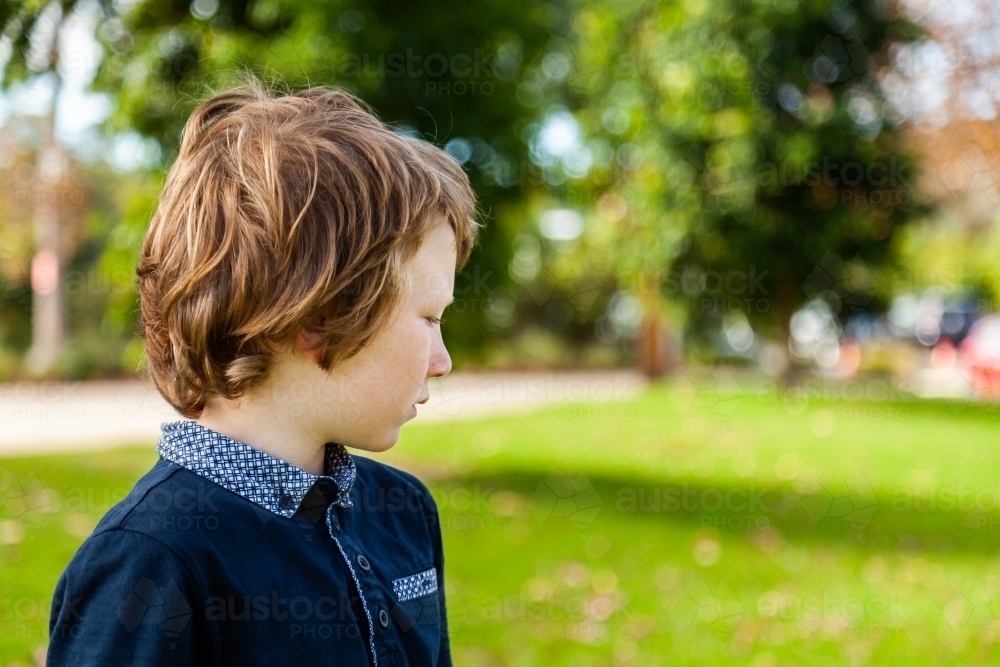 profile of unsure young autistic boy looking to the side at a park outside - Australian Stock Image