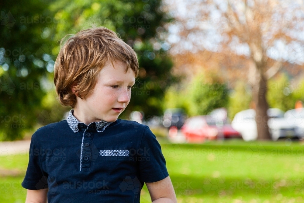 profile of unsure young autistic boy looking to the side at a park outside - Australian Stock Image