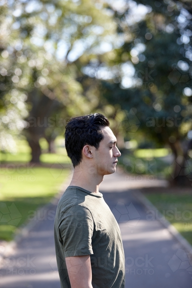 Profile of young man with dark hair standing outside at park - Australian Stock Image