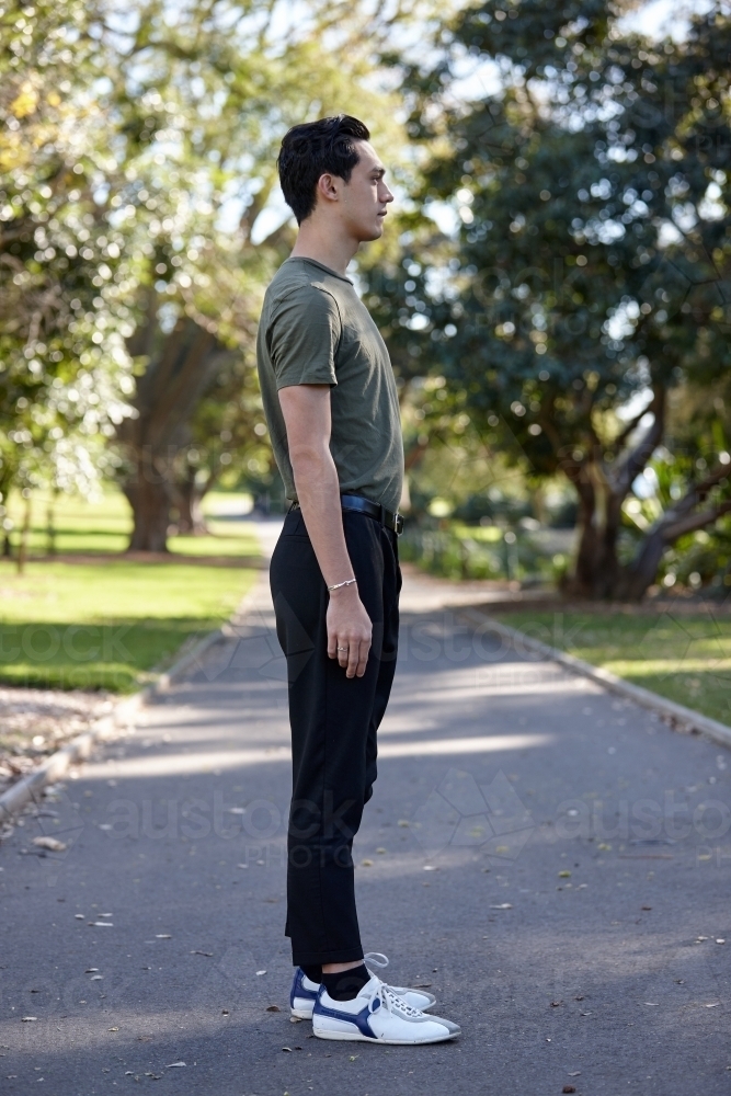 Profile of young man with dark hair standing outside at park - Australian Stock Image