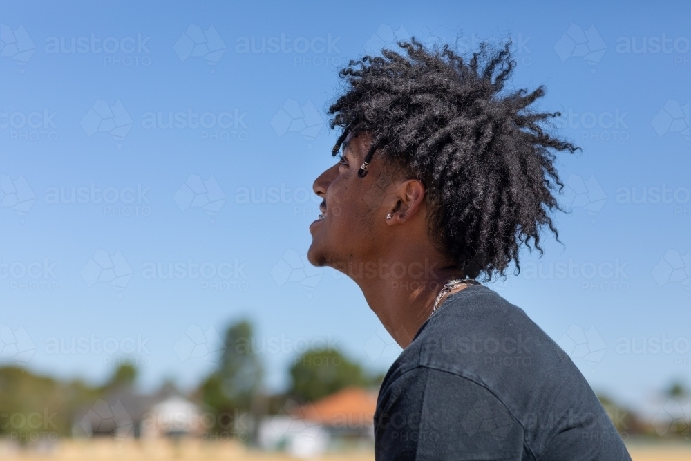 profile of young man with frizzy hair against blue sky - Australian Stock Image