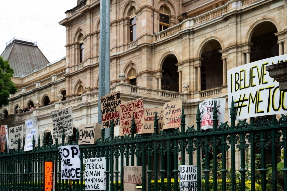 Protest signs on a green wrought iron fence with a grand old sandstone building behind. - Australian Stock Image