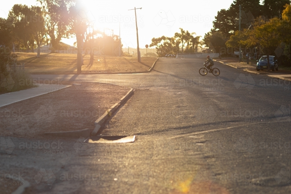 quiet afternoon street with kid on bike crossing road in distance - Australian Stock Image