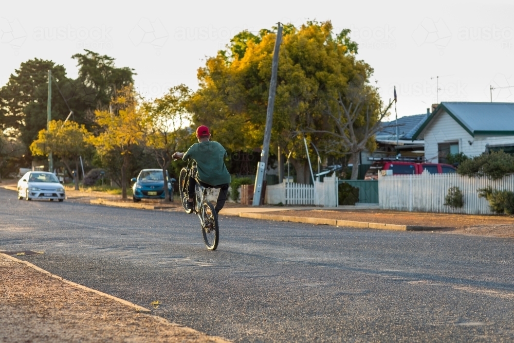 quiet road in country town with kid doing wheelie on a bike - Australian Stock Image