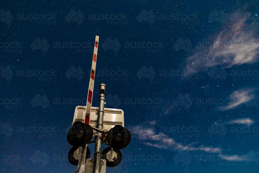 Rail crossing signals and boom barrier against the starry cloudy night sky - Australian Stock Image