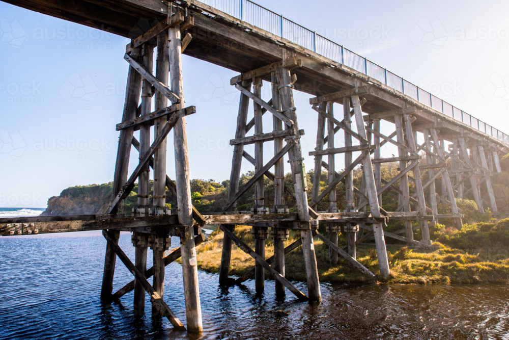 Railway bridge over water with beach in background - Australian Stock Image