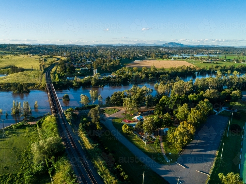 Railway line and bridge over flooding river near park and playground just above floodwaters - Australian Stock Image