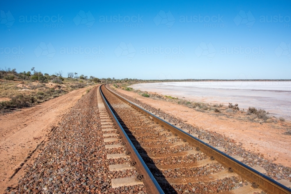 Railway track leading into the distance with salt lake next to it - Australian Stock Image