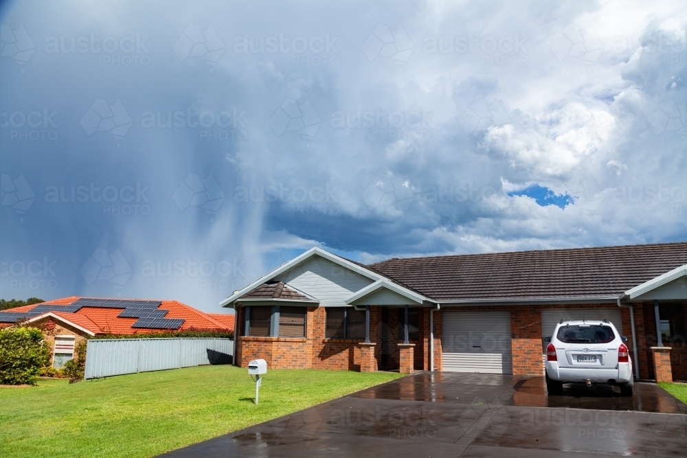Rain and storm clouds in distance behind neat suburban houses - Australian Stock Image